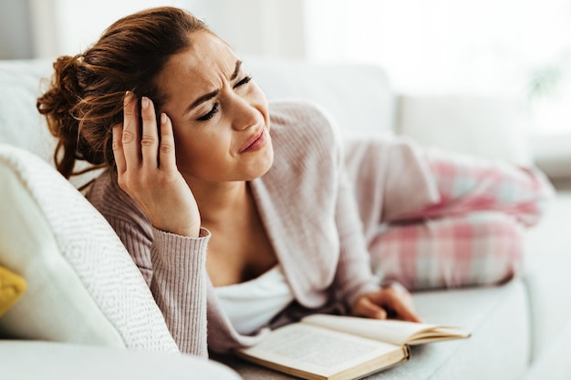 Femme désemparée ayant de forts maux de tête en position allongée sur un canapé à la maison