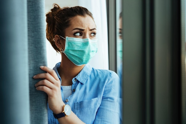 Photo gratuite femme désemparée avec un masque de protection sur son visage regardant à travers la veuve à la maison