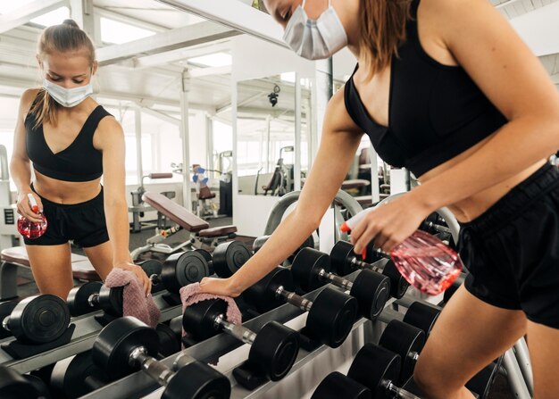 Femme désinfectant l'équipement de gym tout en portant un masque de protection