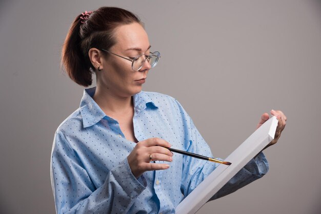 La femme dessine quelque chose dans la toile avec le pinceau sur le gris