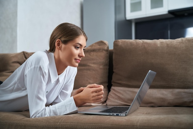 Femme détendue allongée sur un canapé confortable avec un ordinateur portable sans fil