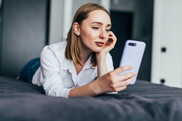 Femme détendue à la maison lisant un message texte dans sa chambre lumineuse