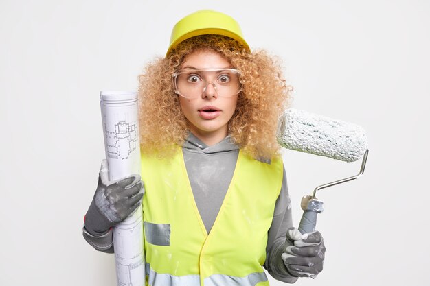 une femme détient un plan et un rouleau propose des travaux de service professionnel dans un appartement nécessitant une peinture fraîche