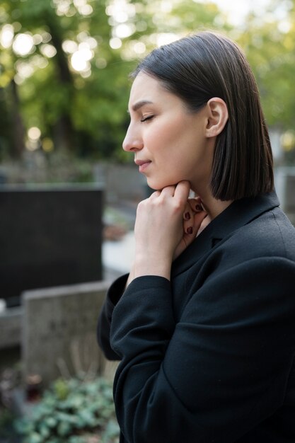 Femme en deuil priant à côté de la tombe au cimetière