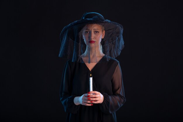 Femme en deuil vêtue de noir avec une bougie allumée sur un bureau noir mort tristesse funérailles