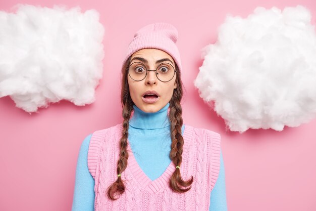 une femme avec deux nattes regarde les yeux obsédés garde la mâchoire baissée porte un chapeau et un gilet isolé sur rose