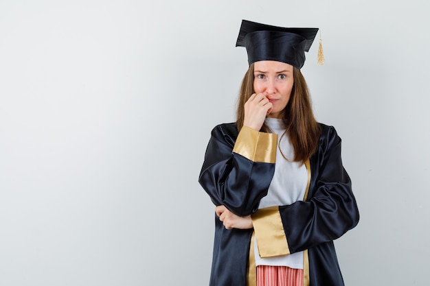 Femme diplômée en gardant la main sur le menton dans des vêtements décontractés, uniforme et regardant anxieux, vue de face.