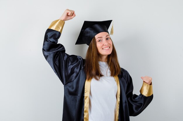 Femme diplômée montrant le geste du gagnant dans des vêtements décontractés, uniforme et à la recherche de bonheur. vue de face.