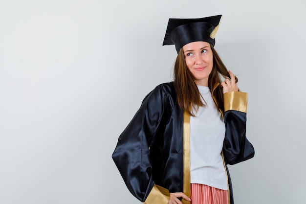 Femme diplômée posant tout en tenant son brin en uniforme, vêtements décontractés et à la rêveuse, vue de face.