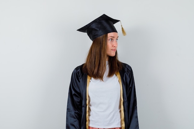 Femme diplômée regardant de côté dans des vêtements décontractés, uniforme et à la recherche concentrée. vue de face.