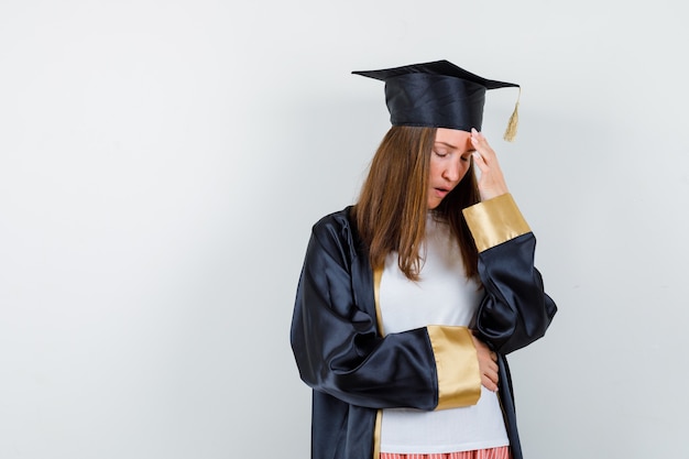 Femme diplômée tenant la main sur la tête dans des vêtements décontractés, uniforme et à la fatigue, vue de face.