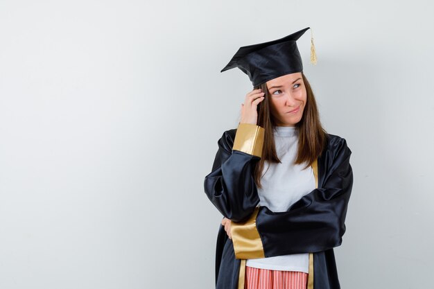 Femme diplômée tenant la main sur la tête dans des vêtements décontractés, uniforme et à la vue de face, hésitante.