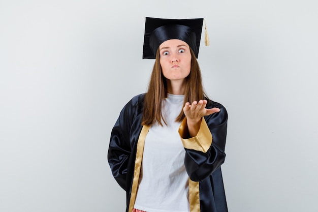 Femme diplômée en uniforme, vêtements décontractés, étirant la main dans le geste de questionnement et à la colère, vue de face.