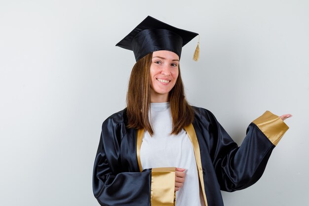 Femme diplômée en uniforme, vêtements décontractés montrant un geste de bienvenue et à la joyeuse vue de face.