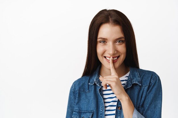 la femme dit un secret et te tais, appuie le doigt sur les lèvres cachant qch, a la surprise, dit de se taire, se tient sur blanc. Espace de copie.