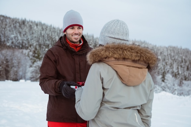 Femme donnant un cadeau à l'homme sur la montagne couverte de neige