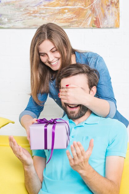 Femme donnant un cadeau surprise à un petit ami qui couvre ses yeux