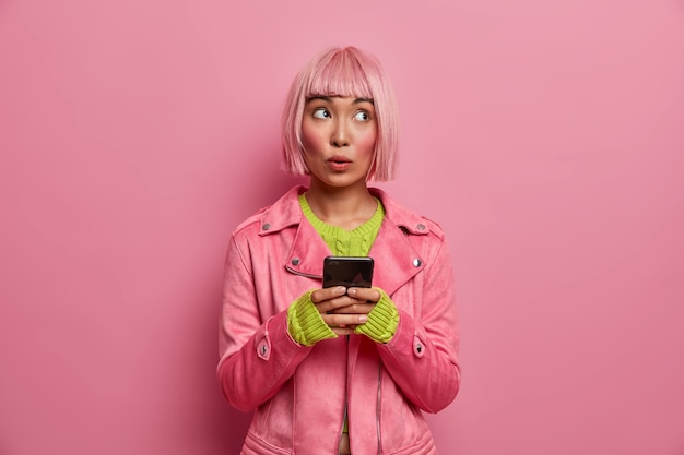 Femme douteuse songeuse avec une coiffure bob, parcourt le fil d'actualité via les réseaux sociaux, détourne les yeux pensivement avec une expression concentrée