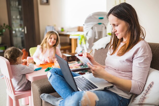 Femme écrivant des notes tout en utilisant un ordinateur portable