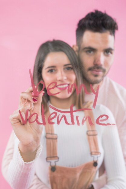 Femme écrivant Sois ma Saint-Valentin sur un verre avec du rouge à lèvres