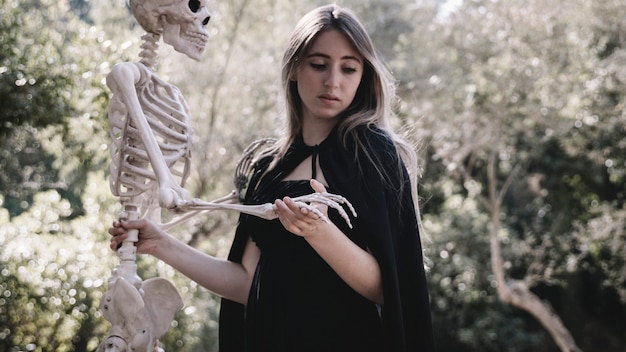 Femme effrayée dans des vêtements de sorcier tenant un squelette