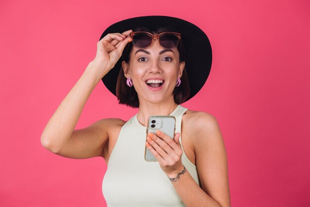 Femme élégante au chapeau et lunettes de soleil sur le mur rouge rose