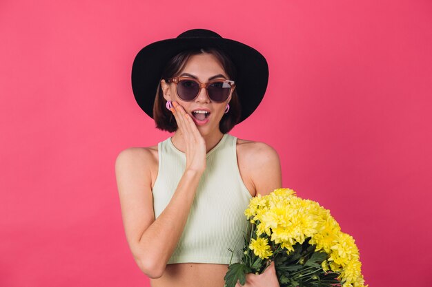 Femme élégante en chapeau et lunettes de soleil, tenant un grand bouquet d'asters jaunes, humeur printanière, émotions émerveillées excitées bouche ouverte espace isolé