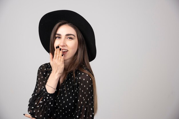 Femme élégante avec un chapeau noir souriant joyeusement.