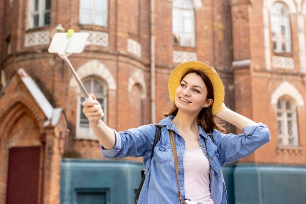 Femme élégante avec un chapeau prenant un selfie à l'extérieur