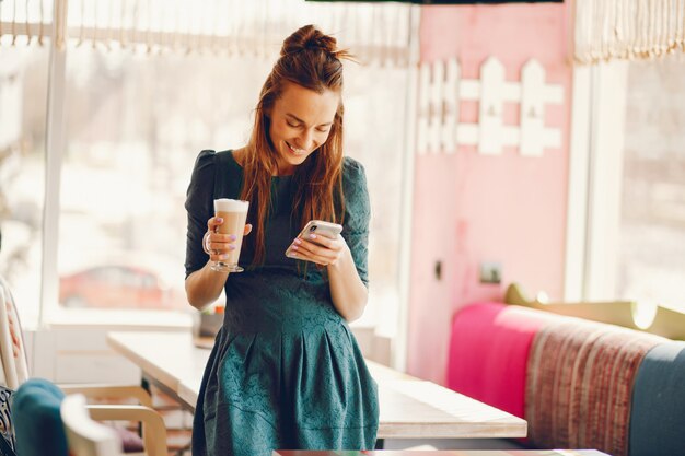 femme élégante avec les cheveux longs et dans une robe verte debout dans un café à la table