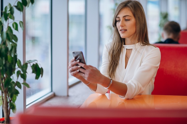 Femme élégante dans un restaurant regardant son téléphone mobile