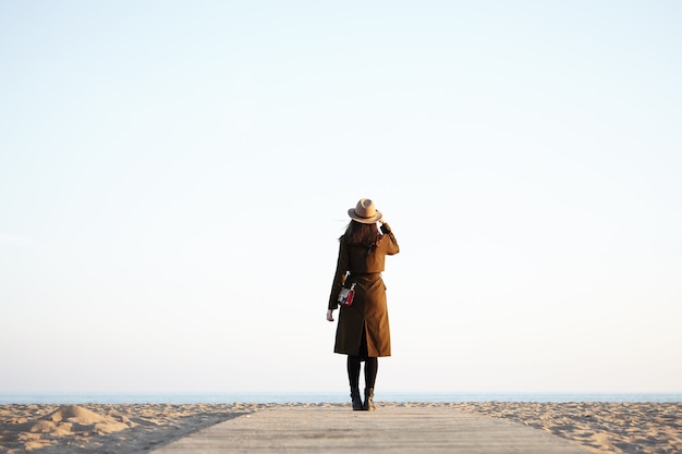 Femme élégante méconnaissable portant un chapeau élégant et un long manteau noir