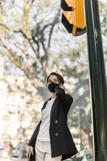 Femme élégante parlant au téléphone à l'extérieur tout en portant un masque médical
