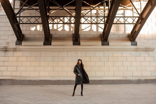 Femme élégante posant en hiver tendance de la mode automne manteau matelassé noir et béret chapeau en cuir dans la vieille belle rue portant des chaussures à talons hauts