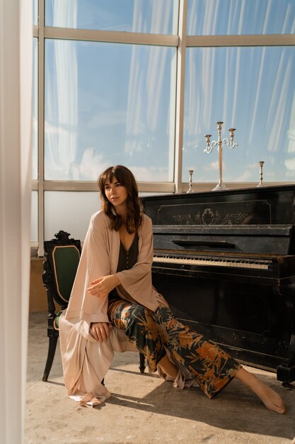 Femme élégante posant près du piano dans une pièce lumineuse élégante.