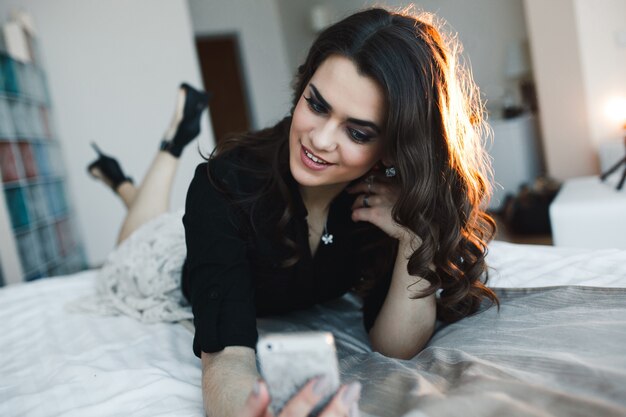 Femme élégante prenant le selfie sur le lit