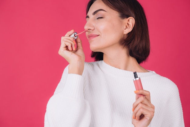 Femme élégante en pull blanc décontracté sur mur rouge rose