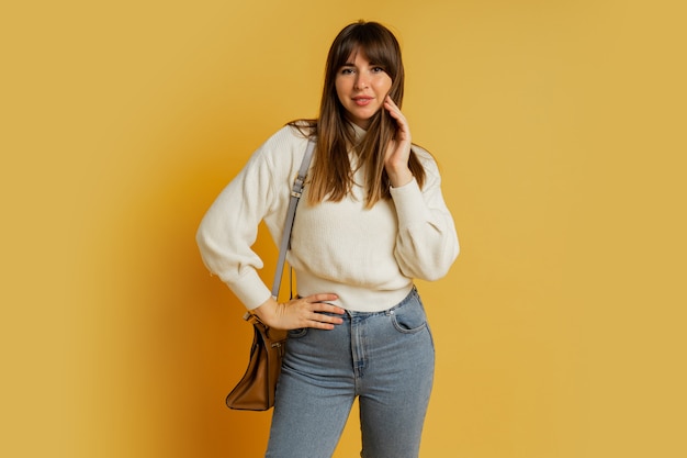 Femme élégante qui pose en studio sur jaune. Porter un pull en laine blanche et un jean.