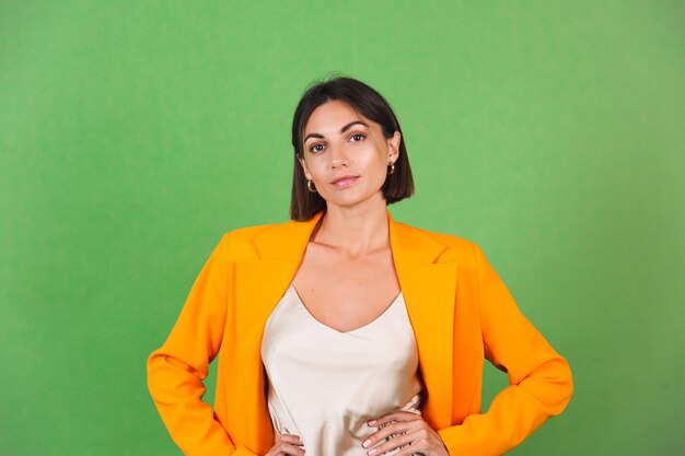 Femme élégante en robe beige en soie et blazer surdimensionné orange sur vert, sourire d'émotions positives