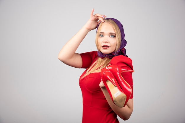 Femme élégante en robe rouge posant avec une paire de talons.