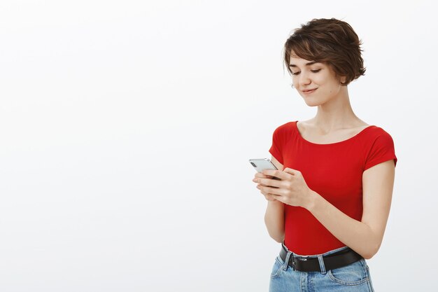 Femme élégante souriante à l'aide de téléphone portable, textos ou navigation sur les réseaux sociaux