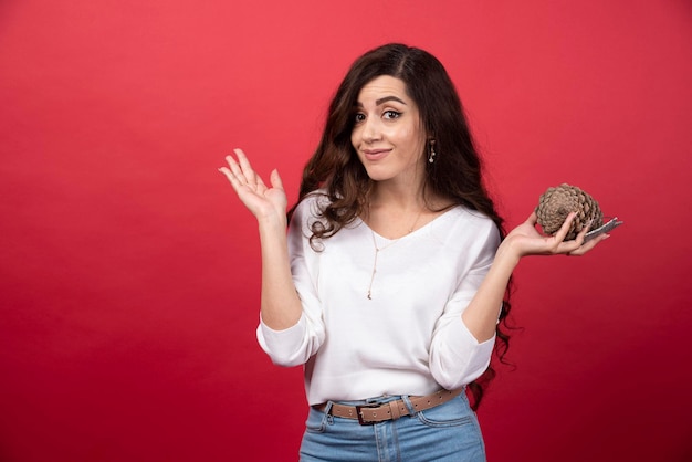 Femme élégante tenant une grosse pomme de pin de Noël sur fond rouge. photo de haute qualité