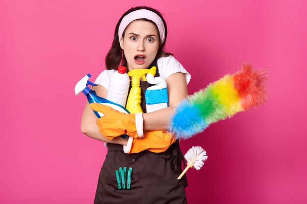 Femme embrasse beaucoup de bouteilles de détergent, plumeau PP, vêtu d'un t-shirt blanc, tablier marron, bandeau