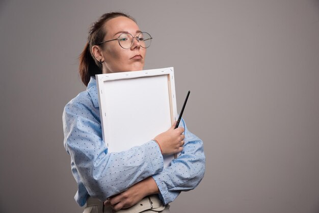 Une femme embrasse une toile vide avec un pinceau sur fond gris