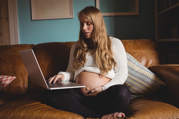 Femme enceinte à l'aide d'un ordinateur portable dans le salon