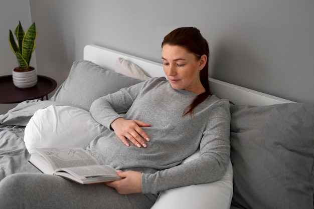 Femme enceinte à angle élevé lisant à la maison