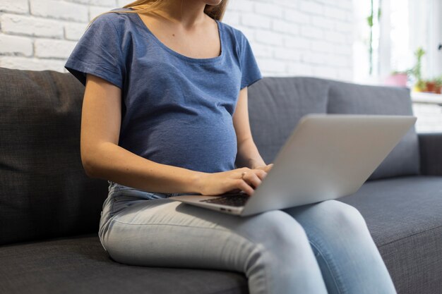Femme enceinte assise sur le canapé et travaillant sur ordinateur portable