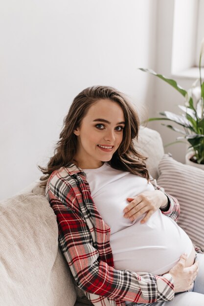 Femme enceinte brune aux yeux bleus sourit sincèrement et regarde devant