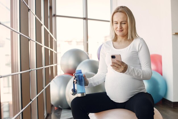 Femme enceinte caucasienne au troisième trimestre à l'aide d'un téléphone tenant une bouteille d'eau