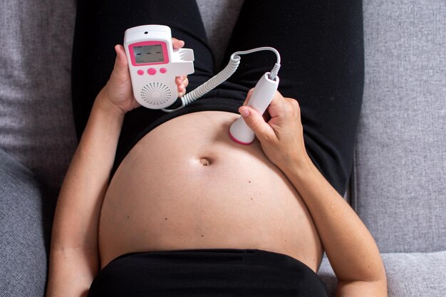 Femme enceinte avec un doppler fœtal écoutant le cœur du bébé assis